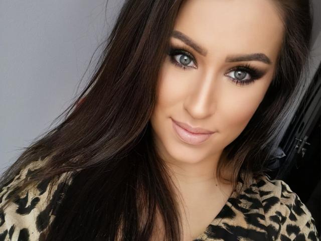 LovelyMichellex69 has blue eyes, dark brown hair, and a smoky eye makeup look with thick eyelashes. She's wearing a leopard print top and smiling softly.