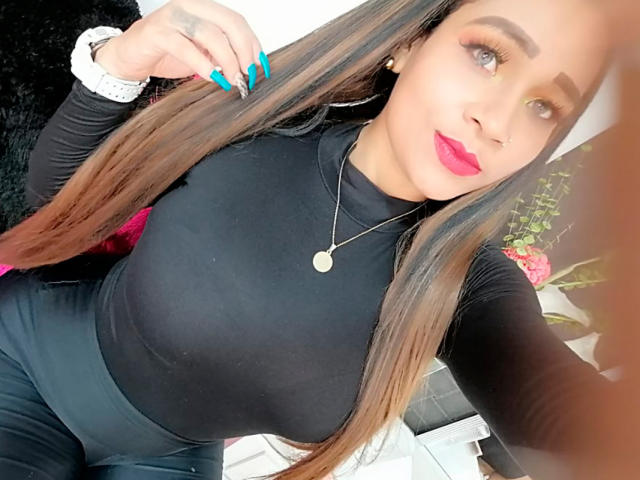 LinaaPrincess with long brown hair, black top, blue nails, pink lipstick, gold necklace, and white watch, showing off her tits and curvy ass.