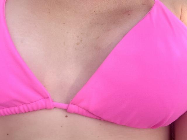 NancyChaude's pink bikini top, showing her small, slightly freckled, and tan-assed tits, with a subtle tan line and a small mole just below her left breast.