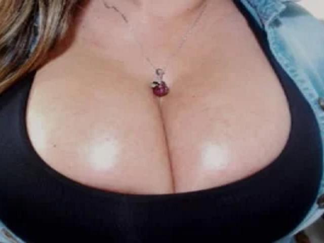 GilliSkquirtty's big, shiny, busty tits in a black tank top with a blue jacket, showing a silver necklace with a red gem.