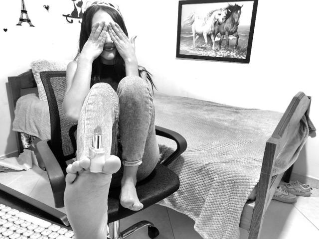 KiriamGomez sitting on a chair, covering her face with hands, wearing jeans and no shoes, showing her bare foot with a small object attached to her sole.