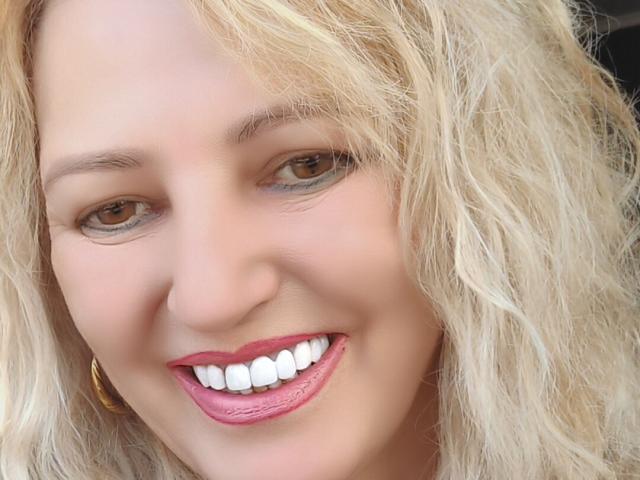 SexyCoco's face, blonde wavy hair, brown eyes, pink lipstick, white teeth, smiling, gold hoop earring, light skin, soft makeup, slightly messy look, close-up, attractive.