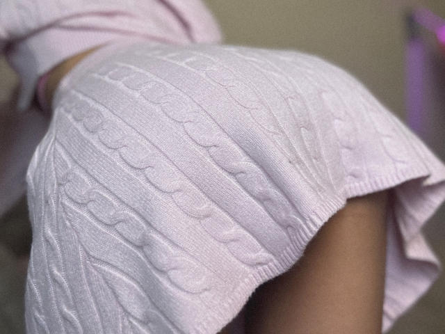 Pingli's butt in a pink, ribbed, cable-knit skirt, showing her curvy, tan-skinned, rounded ass, bent over slightly. Skirt's fabric texture is visible, highlighting her shape.