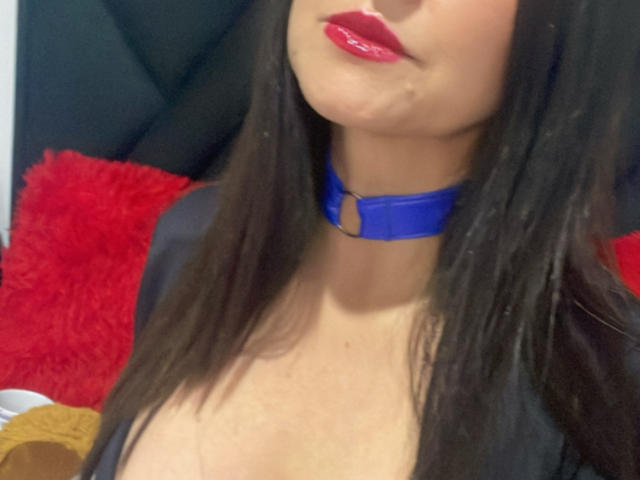 KynkyFetish has glossy red lips, straight black hair, and wears a blue choker with a ring, showing her cleavage and fair skin in a tight shot.