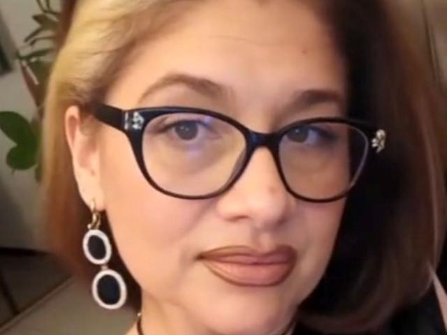 ClassybutNaughty has light skin, brown eyes, and blonde hair. She's wearing black glasses and round earrings with black and white patterns. Her lips are slightly puckered.