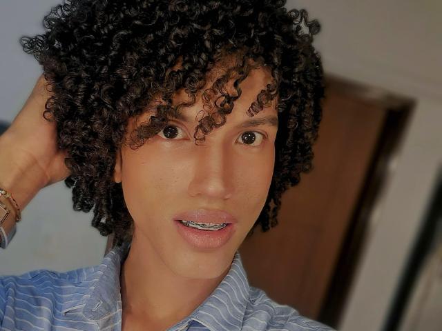 CamilleCedrik has curly black hair, brown eyes, and a light brown skin tone. She's wearing a blue striped shirt, with a bracelet on her right wrist, looking at the camera.