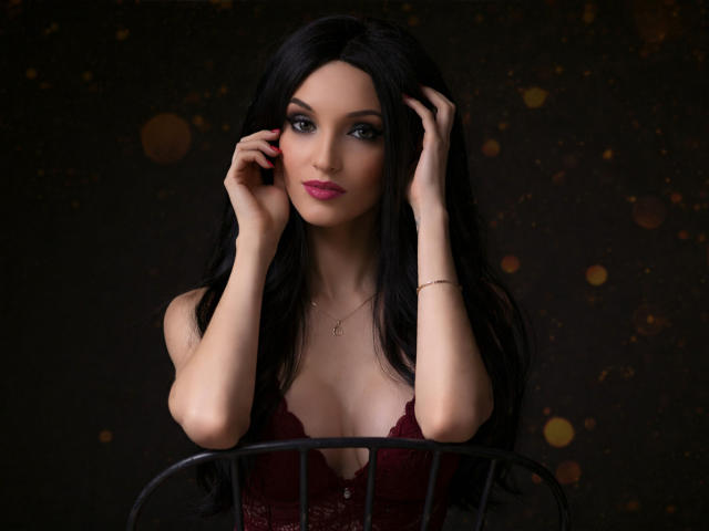 Digital artwork of MaiaMoxie, a sexy woman with long black hair, pale skin, and red lipstick, leaning forward with hands in hair, wearing a low-cut maroon top, dark background. Bokeh lights.