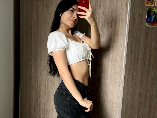 EmilyJensenn with long black hair, white puffy crop top, showing her tits and tight black jeans, taking a mirror selfie with a red phone, holding her ass.