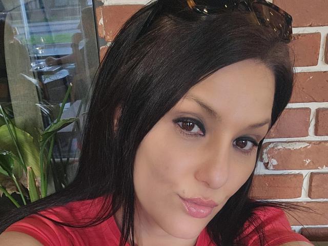 JoliDanielle has black hair, brown eyes, and pink lipstick. She's wearing a red shirt with sunglasses on her head, showing a cute pout. Her tits are slightly visible.
