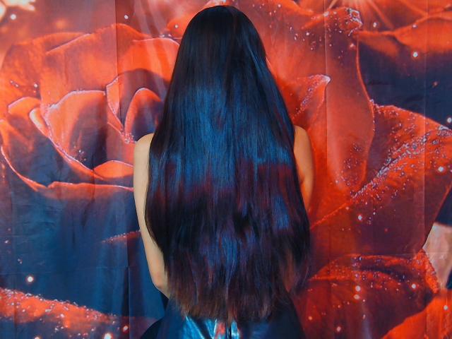 KiriamGomez's dark, shiny, long-ass hair, back to camera, against a giant red rose. Her bare back, small tits, and black dress are visible.