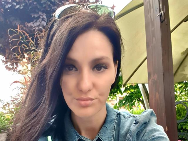 JoliDanielle has dark, wavy hair, brown eyes, and a subtle smile. She wears a denim jacket, with sunglasses on her head, showing a cute, fresh-faced look.