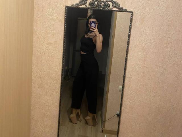 Mirror selfie of AlaneHarradon with black halter top and high-waisted pants, holding phone, standing in wooden room, wearing beige platform heels, medium tits, light brown skin.