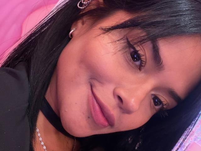 MajoJones has medium brown skin, black straight hair, and a small beauty mark near her right lip. She's wearing a black choker and has long, thick eyelashes.