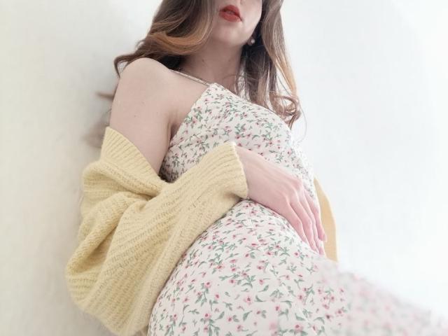 WollyMolly with a floral dress, yellow knitted cardigan, and red lips, holding her tits, lying on a white surface, brown wavy hair, soft light, relaxed pose.