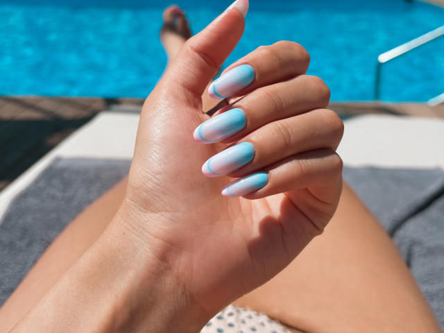 Pingli's hand with blue and pink ombre nails, fingers slightly curled, next to a blue pool. Her tan skin and a gray towel are visible in the background.