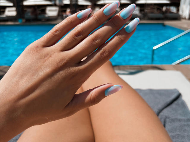 Pingli's hand with blue and pink nail polish, fingers spread, next to her bare ass, by a pool. Her skin is tan, nails are long and glossy.