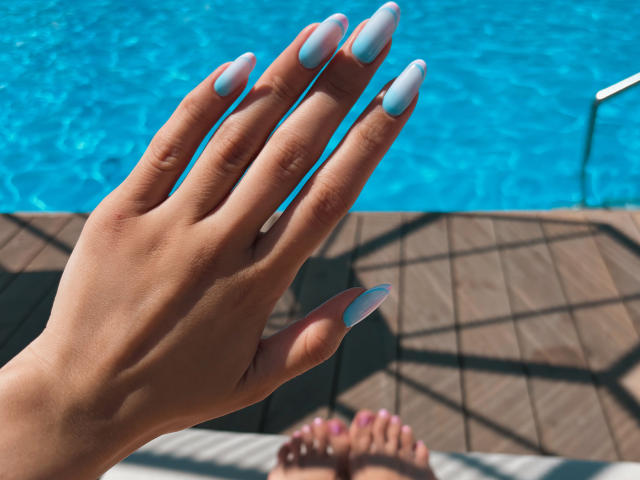 Pingli's hand with light blue, long, almond-shaped nails, showing off her smooth, tan skin, is in the foreground. Her toes with pink nail polish are in the background.