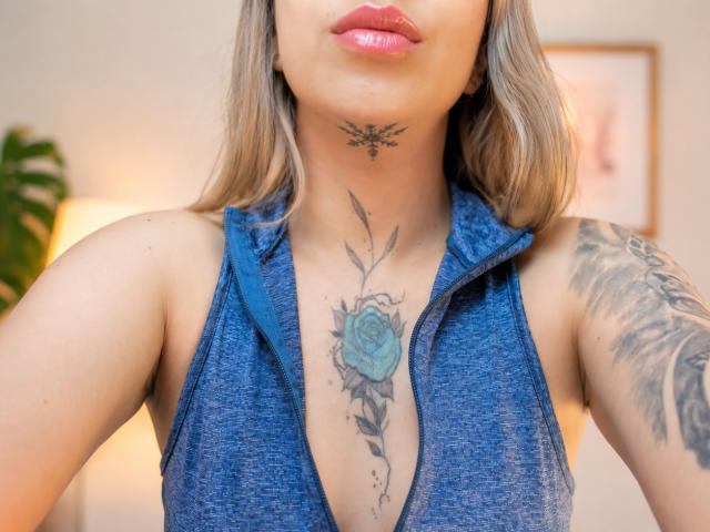 KayleeM has a blue rose tattoo on her chest, a snowflake tattoo on her neck, and a sleeve tattoo on her right arm, wearing a blue sleeveless top.