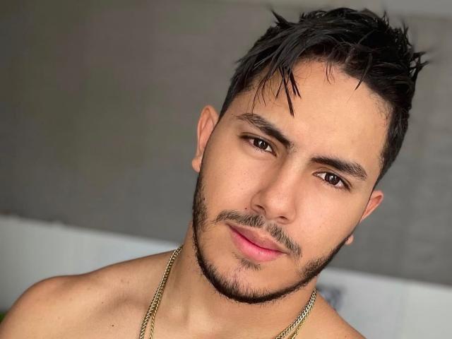 OwenPierce has a sexy, clean-shaven face with dark, short hair, a thin mustache, and brown eyes. He's shirtless, wearing a gold chain, and has a slight smirk.