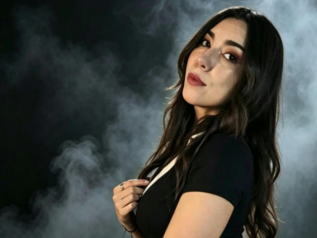 MiaReed with long dark hair, black top, holding straps, looking over shoulder, slight smile, smoky background, her tits subtle, cute, soft makeup, slightly wavy hair, confident.