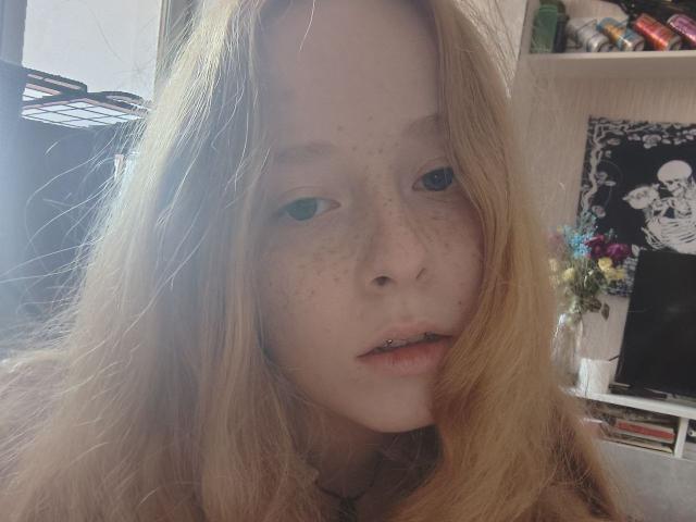 MichaelEuber has long, blonde hair, blue eyes, and freckles. He's looking at the camera with a slight, open-mouthed, pouty expression, showing a small, silver lip piercing.