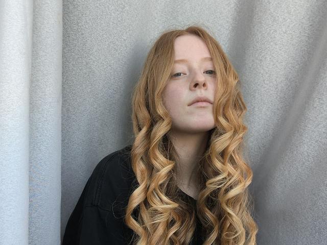 MichaelEuber has long, wavy, blonde hair, pale skin, and a neutral expression, wearing a black shirt. Her nose is slightly upturned. Her tits are small, barely visible.