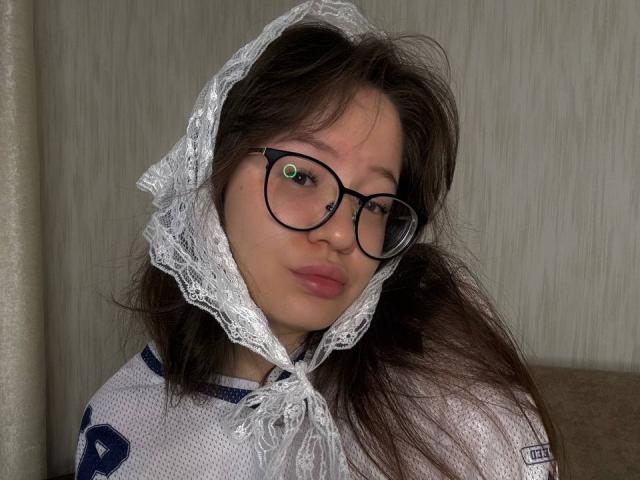 LauriceWesberry with glasses, lace headscarf, and sports jersey, showing pouty lips and green eyes, has brown hair and a cute, nerdy look, with a slightly messy hairstyle.