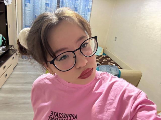 LauriceWesberry, wearing a pink shirt and black glasses, with her brown hair in a bun, pouty red lips, and a cute face, taking a selfie.