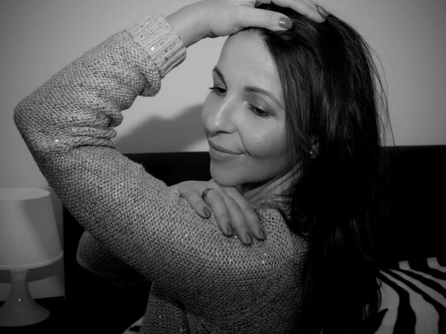 Aprel's got long dark hair, wearing a textured knit sweater, smirking with her hand in her hair, showing a ring on her finger, and a cute ass. Black-and-white photo.