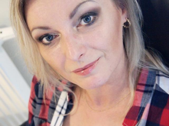 XLovelyVanessa with blonde hair, blue eyes, and glossy pink lips, wearing a red plaid shirt, has a cute smile, and gold hoop earrings, in a selfie.