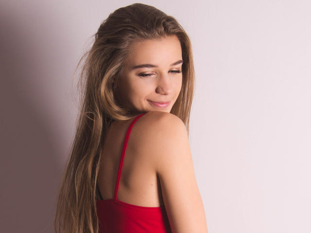 LucyBestCandy with long brown hair, red spaghetti strap top, smiling slightly, looking over her shoulder, showing her bare back and smooth skin. Her tits are small and cute.