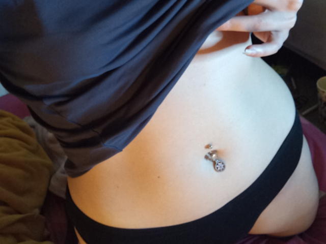 VirginieFrancaise's bare belly with a silver navel piercing, black panties, and a lifted gray shirt, showing her soft, pale skin and slightly curvy, smooth-ass.