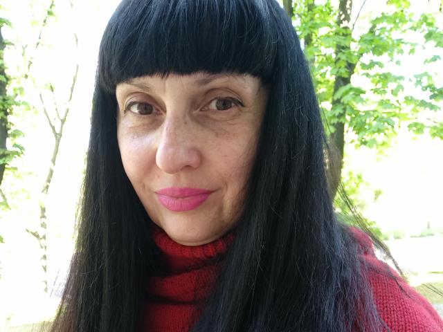 MelanyBanks has dark black hair with bangs, pink lipstick, and is wearing a red turtleneck, looking straight at the camera with a slight smile. Her ass is not visible.