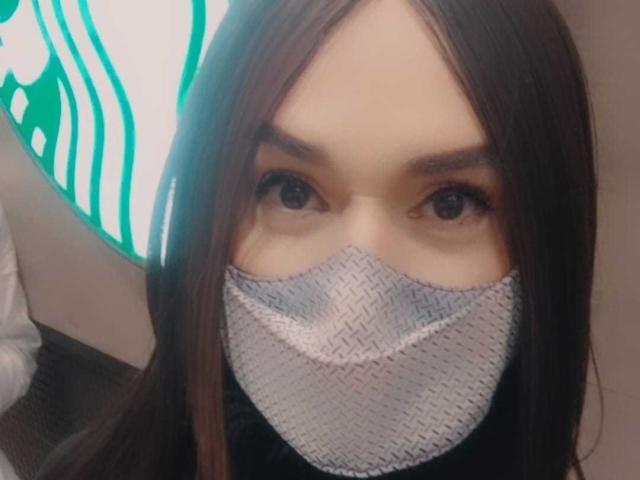 Jhovanna, qui a les cheveux bruns, porte un masque facial tressé qui couvre son nez et sa bouche. Elle a les yeux bruns et regarde la caméra. Son masque est gris et a une texture tressée..