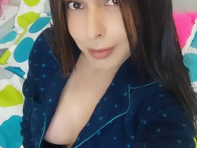 Jhovanna, avec ses yeux marron, ses longs cheveux noirs et ses lèvres roses, porte une robe bleue à pois, laissant entrevoir sa poitrine, et regarde la caméra. Ses seins sont partiellement visibles..