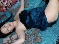 MarleneDavies lying on a bed, wearing a black lace strap and blue satin panties, showing her ass and small tits, with dark hair and a relaxed expression.