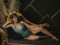 JuliaNewell, with tan skin and dark curly hair, lounges on a gold ornate couch in a blue lace bodysuit, showing her tits and pussy, with black fur and puffs.