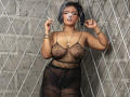 AliceJelanni, sexy, curvy, tan-skinned woman with large breasts, wearing sheer black lingerie with star patterns, standing against a diamond-patterned wall, biting her finger, gold jewelry, seductive pose.
