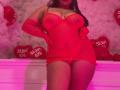LolyMarce in red, sheer, sparkly lingerie with matching gloves, exposing her big, shiny tits and a little of her pussy. She's standing, hands on hips, with a sexy look.