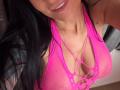 AndraD's pink fishnet top with large cutouts reveals her big tits, showing her cleavage and part of her smiling face with dark hair. AndraD has a small mole on her right arm.