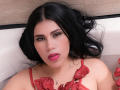 AgathaPember with black hair, pink lipstick, and red rose petals on her chest, lying in a bathtub, looking directly at the camera with a slightly open mouth.