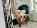 LauraineX, topless with tits, wearing black fishnet stockings, black garter, and black lace, is on a green velvet bed, legs spread, hand on her pussy, head back.