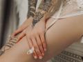 SophieKitty's hands with tattoos resting on her white lace-covered pussy, showing off a ring and delicate nails. Her pale skin contrasts with her dark ink.