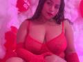 LolyMarce with curly brown hair, red bra, and red glittery gloves, showing her big tits, sitting on pink and white fluffy stuff, surrounded by red heart balloons.