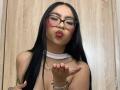ChloeMoretti with long black hair, glasses, nose ring, and pink lipstick, pouting, holding her hand up, showing her nails, wearing a white choker and gold necklace.