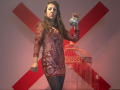 MaitresseElsa with long brown hair, wearing a red, floral, sheer dress, holding a silver mirror ball, standing in front of a red birdcage, looking serious.
