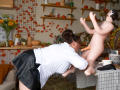 BerryChic with brown hair in a bun, white shirt, and black skirt, bent over, using a dildo on a pink, lifelike doll with no clothes, in an autumn-themed room.