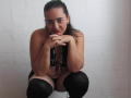 SaimaJaye69, topless with black lingerie, crouching, hands under chin, black thigh-highs, dark hair in a ponytail, subtle smile, white textured wall in background.