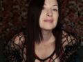 MarleneDavies with dark brown hair, light skin, and green eyes, wearing a black netted top with red straps, has a small bruise on her chest, looking up.