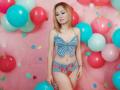 SpermeMangerTS with light skin and straight blonde hair, wearing a blue butterfly top and red butterfly-patterned blue denim shorts, surrounded by colorful balloons and confetti, standing confidently.